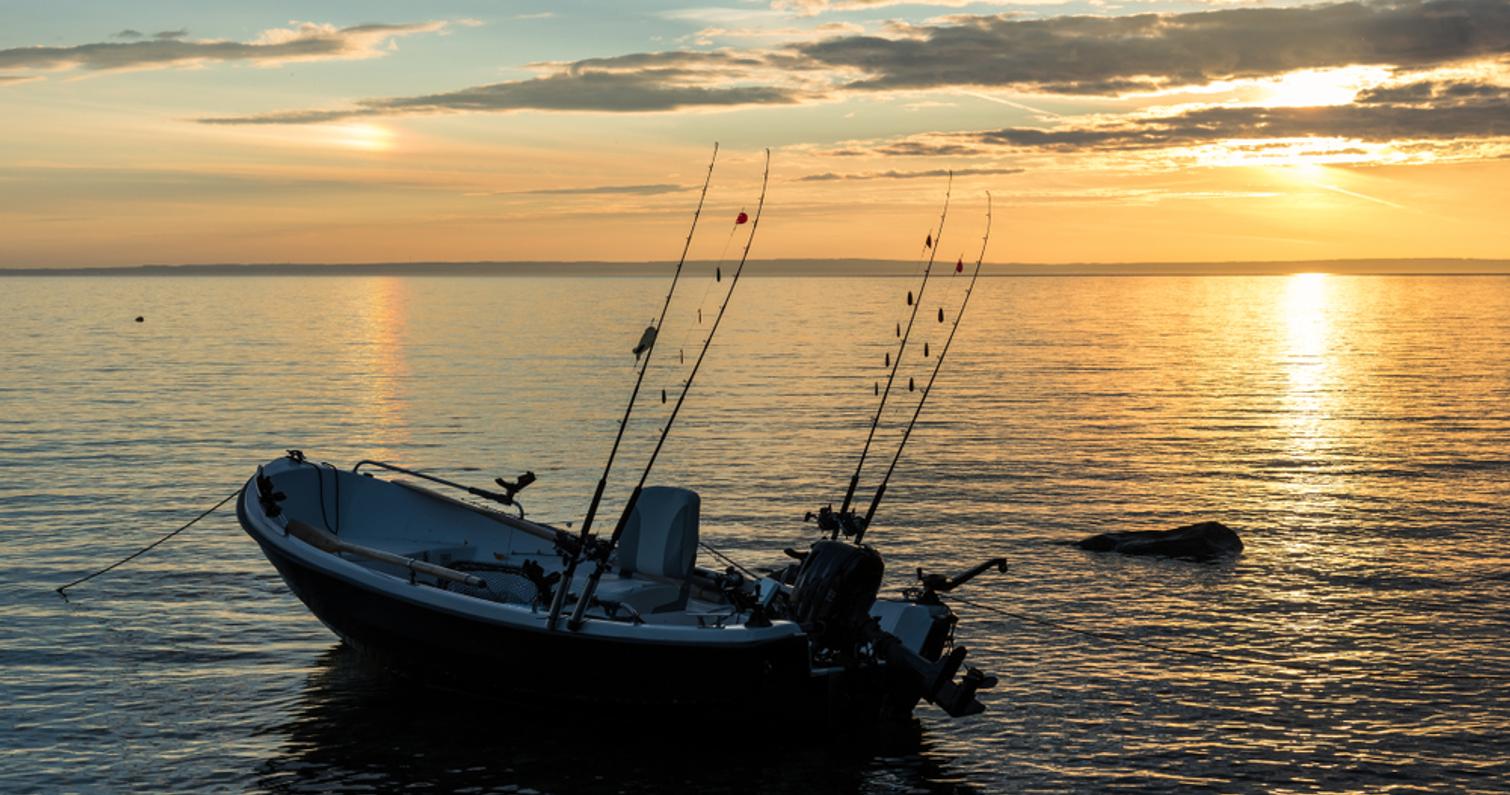 Kalastusvene vesillä oranssissa auringonlaskussa.