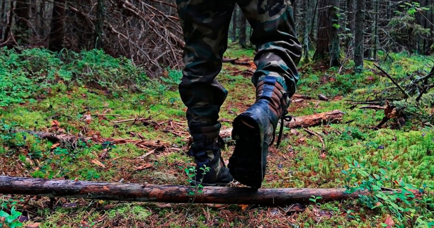 Erävarusteisiin pukeutunut henkilö kävelee metsässä.